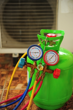 Green refrigerant cylinder with manifold gauge set connected, showing blue, red, and yellow hoses for diagnostics.