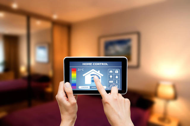 Tablet displaying smart home dashboard with temperature control and automation icons in modern bedroom.
