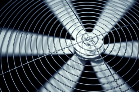 Close-up of spinning fan blades behind concentric metal grille, showing dynamic airflow and industrial design.