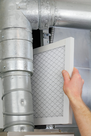 Hand inserting rectangular air filter into galvanized ductwork of HVAC system during routine maintenance.
