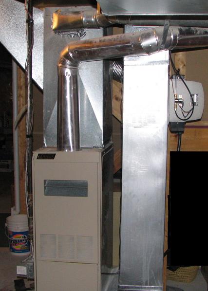 Beige forced-air furnace with vented front panel, galvanized steel ductwork, and metal exhaust pipes in basement.