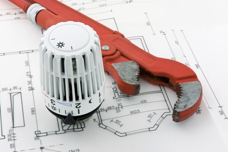 Red pipe wrench and white radiator valve placed on architectural blueprints showing floor plans and measurements.