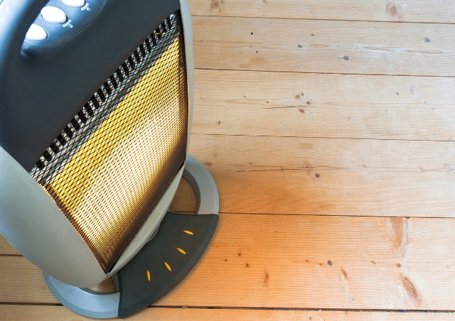 Electric space heater glowing on wooden floor, with visible heating elements behind mesh screen.