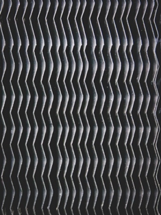Close-up of textured surface with repeating zigzag ridges, possibly part of a heat exchanger or filter.