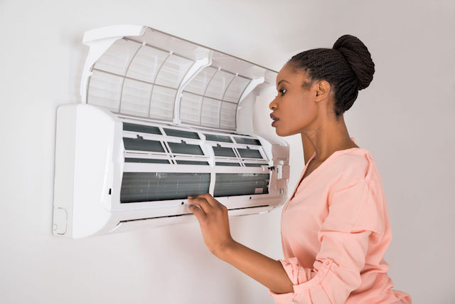 Person examining internal components of wall-mounted AC unit with open panel revealing filters and coils.