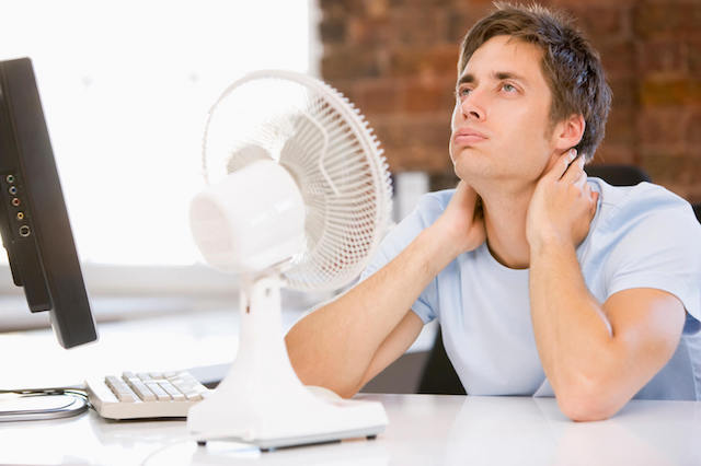 Warm indoor scene with person seeking comfort from fan, emphasizing cooling solutions and summer prep.