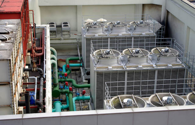 Large rooftop HVAC system with cooling towers, axial fans, and multicolored piping for heat dissipation.