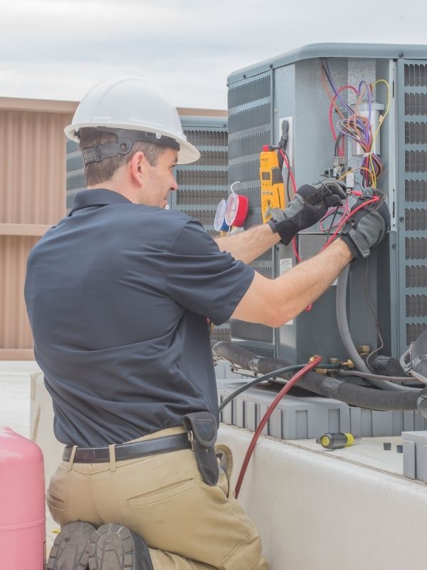 An HVAC technician checking an outdoor condenser. 