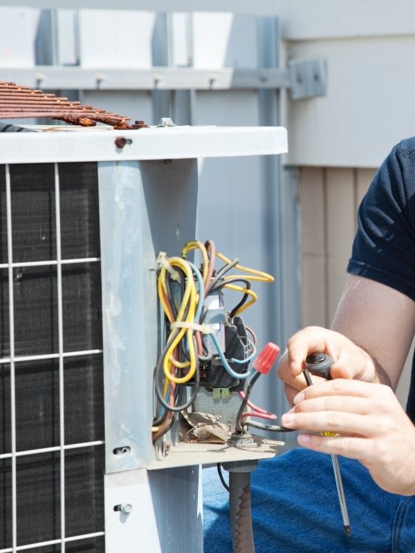An HVAC technician checking an outdoor air conditioning unit.